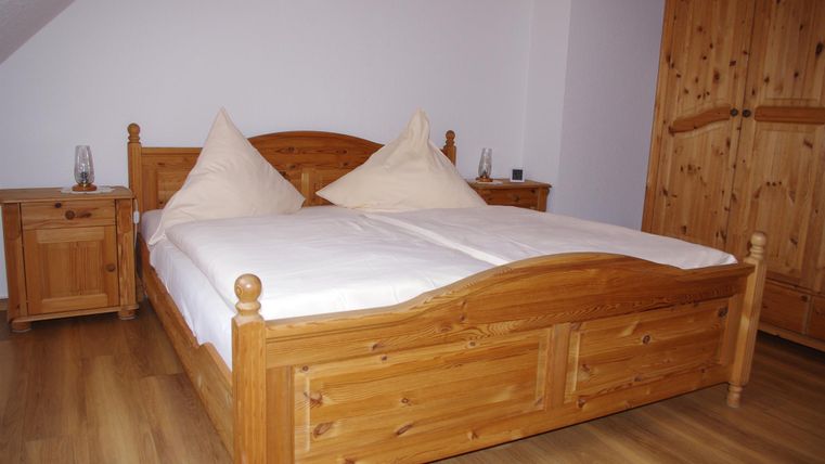 Ein gemütliches Schlafzimmer mit einem großen Doppelbett aus Holz. Neben dem Bett stehen Nachttische und ein Holzschrank.