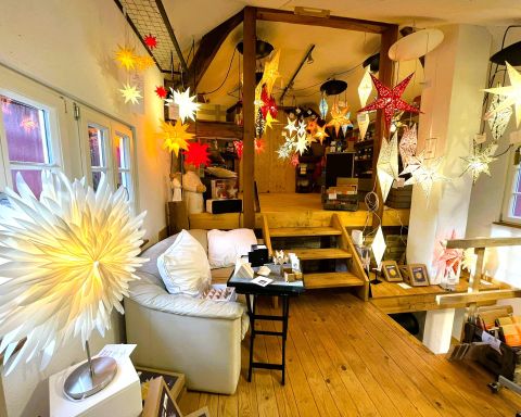 Een gezellige kamer met een houten vloer, die feestelijke lichtjes en decoraties toont. Op de voorgrond staan een comfortabele bank en een tafel met verschillende spullen.