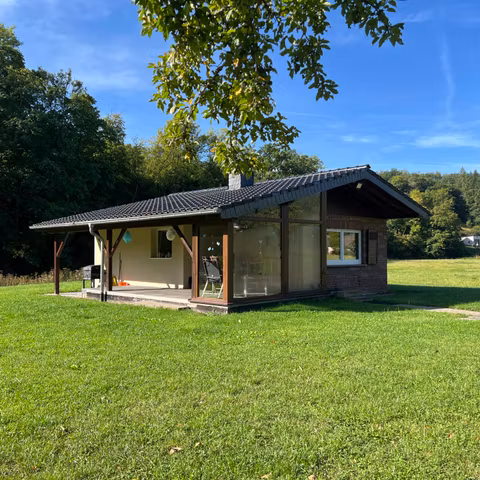  une maison moderne au milieu d'une prairie verte. Le ciel est dégagé et les environs sont entourés d'arbres.