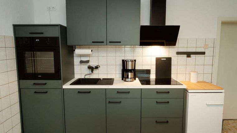 Une cuisine moderne avec des meubles verts et des murs blancs. Elle contient une cuisinière, un réfrigérateur et une machine à café.