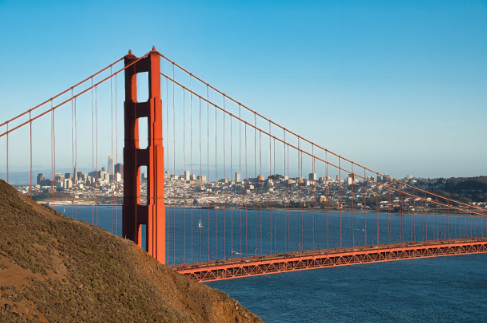 Eine beeindruckende Aussicht auf die Golden Gate Bridge mit der Stadt San Francisco im Hintergrund. Der klare Himmel und die ruhige Wasseroberfläche sorgen für eine malerische Kulisse.