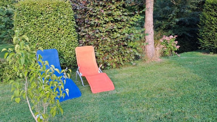 Two loungers in a green garden, one blue and one orange.
Surrounded by trees and bushes, ideal for relaxing.