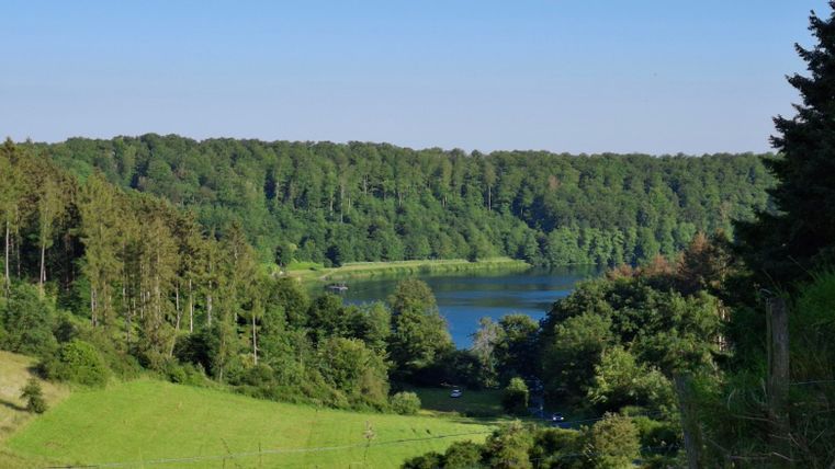 Eine malerische Landschaft mit einem ruhigen See und umliegenden Wäldern. Der Himmel ist klar und die Vegetation ist üppig grün.