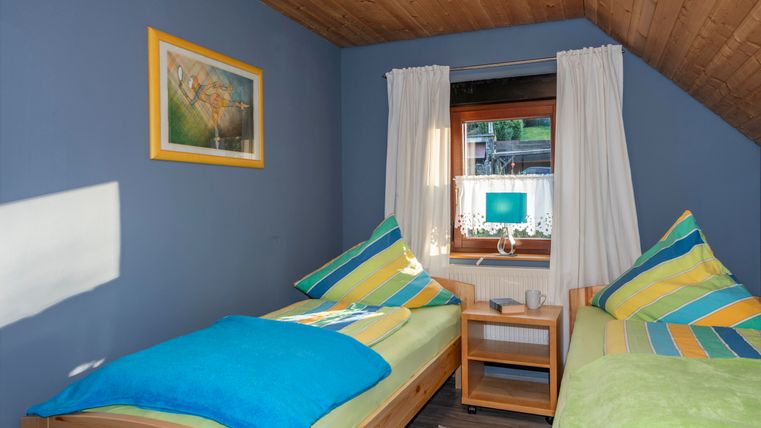 Een gezellige kamer met twee bedden en kleurrijke kussens. Het raam laat veel daglicht binnen en biedt uitzicht naar buiten.