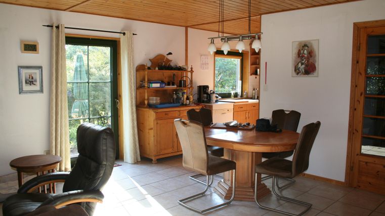 Een gezellige woonruimte met een ronde tafel en stoelen. Op de achtergrond bevindt zich een open keuken met houten planken.