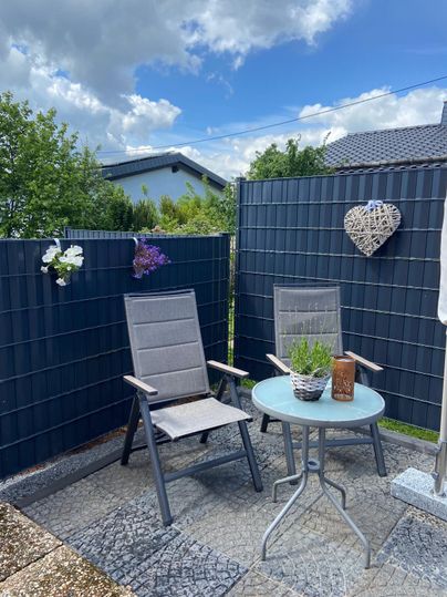 A cozy terrace with two chairs and a table. In the background, green plants and a heart made of decorations can be seen.