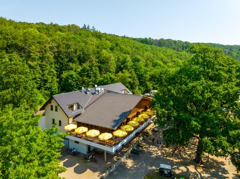 Un restaurant acogant entouré d'arbres verts. Sur la terrasse, des parasols jaunes invitent à la détente.
