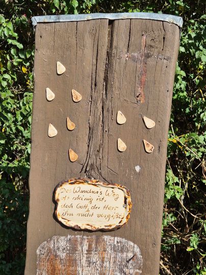Ein Holzschild mit verschiedenen Steinen, die wie Regentropfen angeordnet sind. Darunter steht eine kleine, handgeschriebene Nachricht.