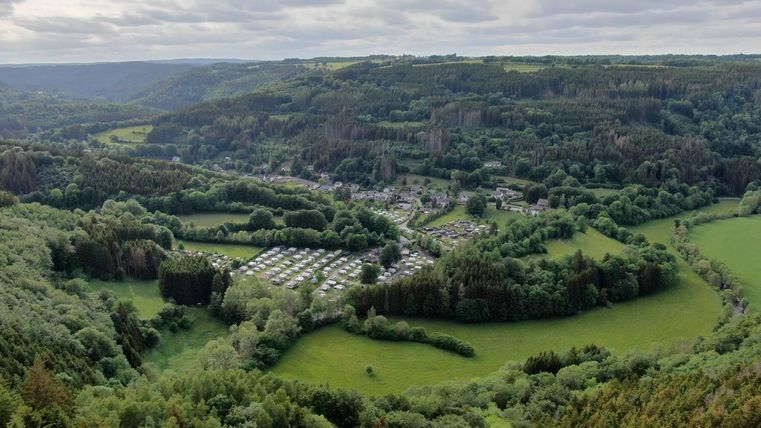 Une paysage impressionnant avec des collines verdoyantes et un petit village dans la vallée. Au premier plan, on peut voir des terrains de camping et des prairies, entourés de forêts denses.