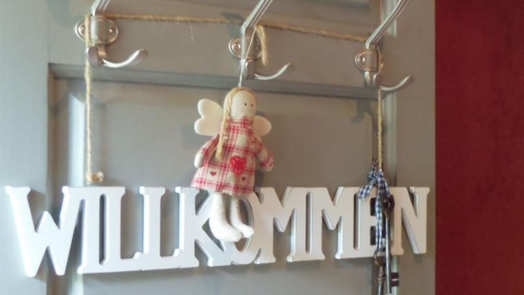 Eine dekorative Garderobe mit dem Wort "WILLKOMMEN" und einem kleinen Engel. Es hängen auch einige Schlüssel an den Haken.