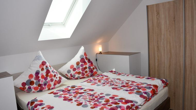 A cozy bedroom with a double bed and colorful pillows. The room has a skylight and modern wooden furniture.