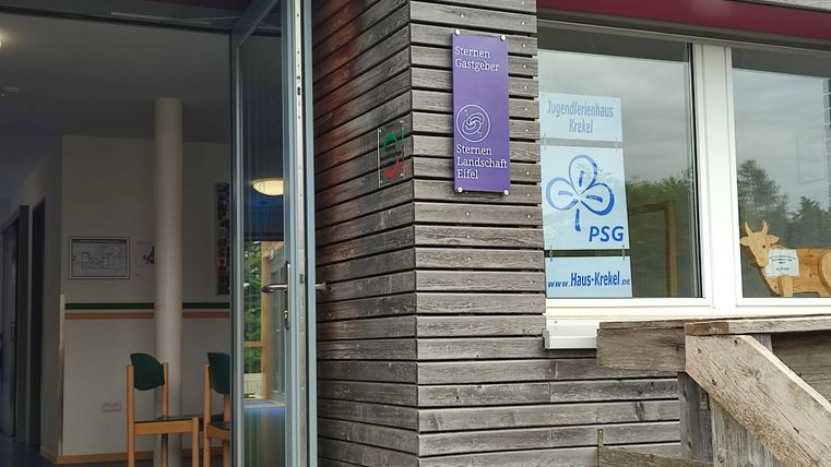 Un bâtiment moderne avec un revêtement en bois et une zone d'entrée. Les fenêtres affichent différentes enseignes et une invitation.