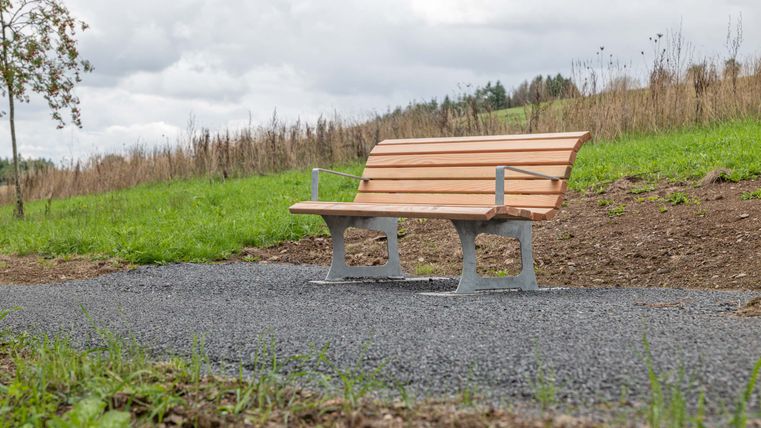 A wooden bench on a stone path, surrounded by meadows and fields