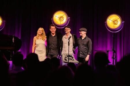 A singer in a glittering suit stands on stage and sings. Next to him, a pianist sits at the piano and accompanies him.
