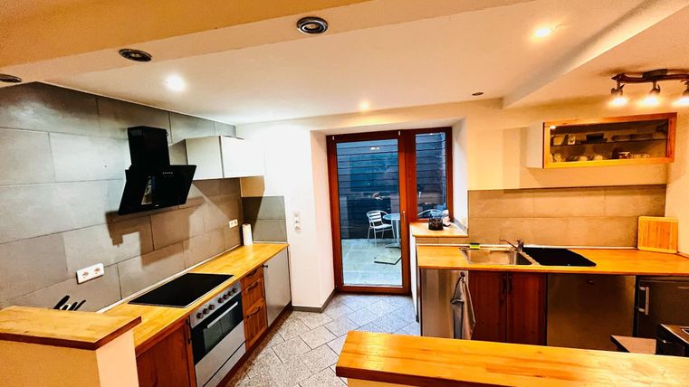 Een moderne keuken met houten en stenen oppervlakken. De grote ramen bieden uitzicht op een buitenruimte met zitgelegenheid.