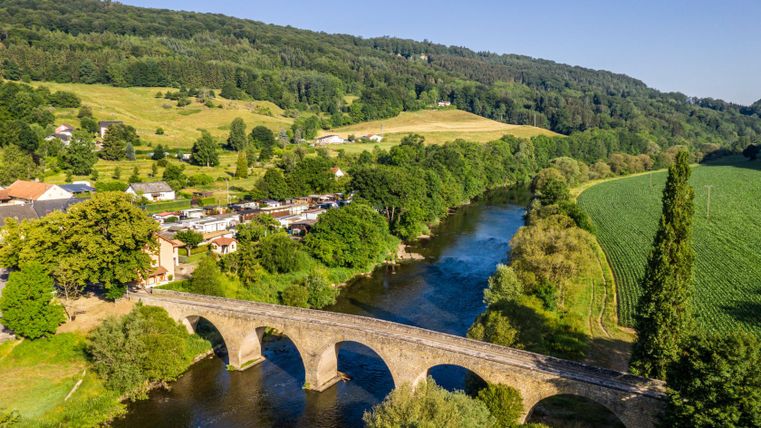 Luchtfoto van een stenen brug over een rivier, omgeven door groene velden en bossen.