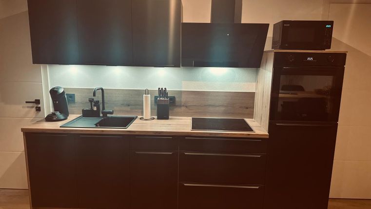 Eine moderne Küche mit dunklen Schränken, einem Herd und einem Kühlschrank. Die Beleuchtung sorgt für eine angenehme Atmosphäre.