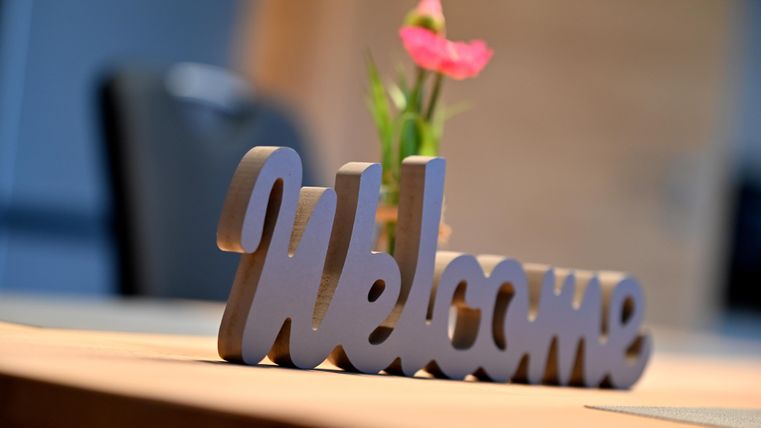 Ein Tisch mit einem „Welcome“-Schild und einer kleinen Blume. Die Atmosphäre ist einladend und freundlich.