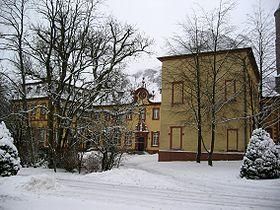 Un bâtiment historique entouré d'arbres recouverts de neige. La scène dégage une atmosphère hivernale paisible.