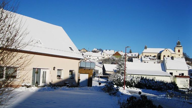 Un paysage enneigé avec de belles maisons et un ciel bleu clair. À l'arrière-plan, une église est visible.