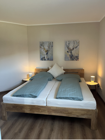 Une chambre moderne avec un lit double et deux tables de nuit. Des œuvres d'art sont accrochées aux murs, et la pièce a une atmosphère lumineuse et accueillante.