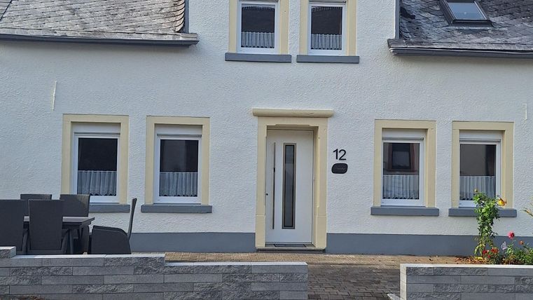 Een uitnodigend, tweelaags huis met lichte muren en een zadeldak. De ramen zijn symmetrisch gerangschikt en er is een klein tuingebied voor het huis.