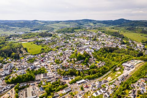 Eine luftige Ansicht einer kleinen Stadt umgeben von grünen Hügeln und Wäldern. Die Stadt hat zahlreiche Gebäude und Straßen, die sich harmonisch in die Landschaft einfügen.