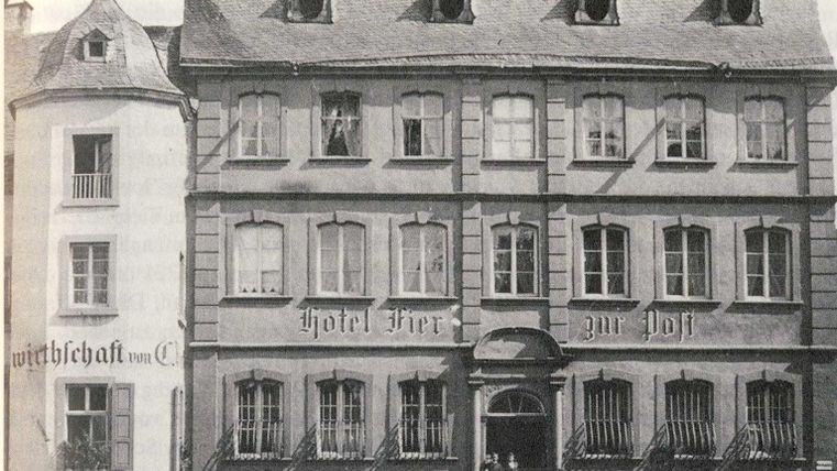 Ein historisches Gebäude mit der Beschriftung "Hotel zur Post". Vor dem Hotel stehen mehrere Personen.