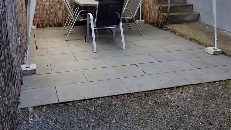Een klein tuingebied met een witte paviljoen en een tafel met stoelen. De grond is bedekt met platen en grind.