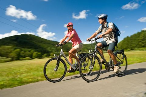 Een paar fietst samen op een pad door een groene landschap. De lucht is blauw met een paar wolken.
