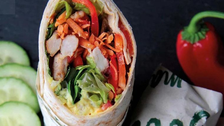 A delicious wrap with chicken, fresh vegetables, and a colorful filling. Served with a few cucumber slices and a red bell pepper.
