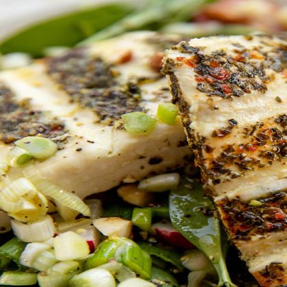 Ein Stück gegrillter Brat und Grillkäse mit Kräutern liegt auf einem Bett aus frischem Gemüse. Die Farben der Zutaten sind frisch und einladend.