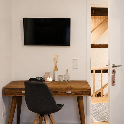 A modern room with a wooden table and a television on the wall. The door leads to another room with visible wooden structures.