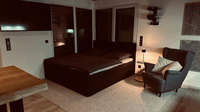 Une chambre confortable avec un grand lit et un fauteuil confortable. L'atmosphère est chaleureuse et accueillante, avec un éclairage doux.