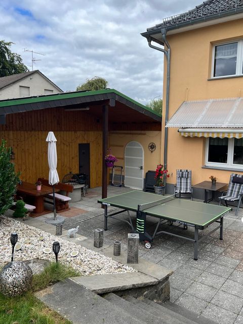 Un patio confortable avec une table de ping-pong et un pavillon en bois. La zone est entourée de plantes et d'une maison lumineuse.