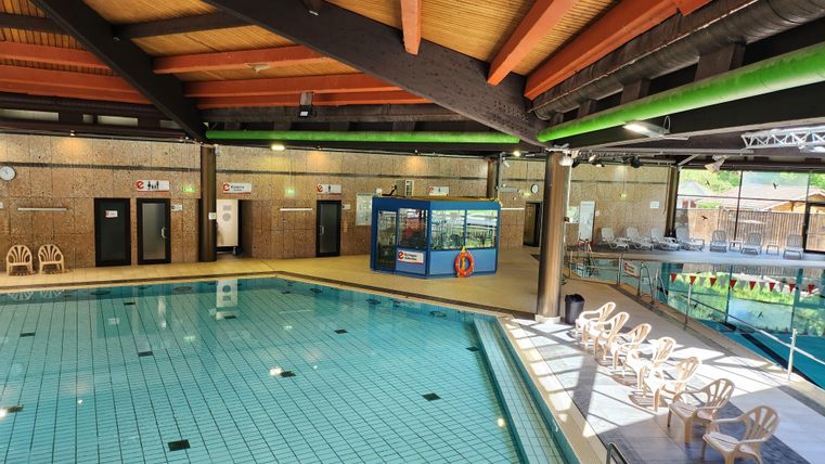An indoor pool with crystal clear water and wooden ceilings. Comfortable chairs are placed on the side and a small aquarium area is visible.
