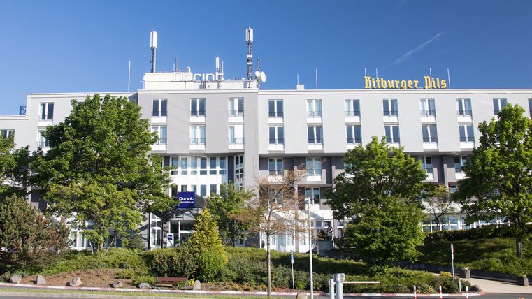 Un bâtiment d'hôtel moderne avec de nombreuses fenêtres et un ciel bleu clair. Entouré d'arbres verts et d'un terrain bien entretenu.