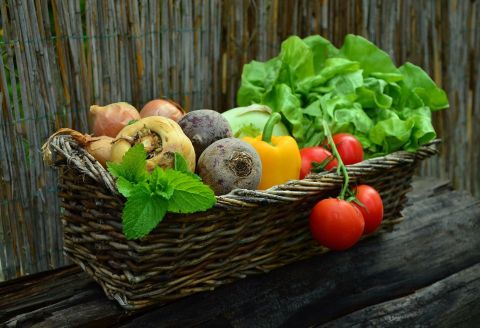 Symbolbild-Auf einem alten Holzbalken steht ein viereckiger, geflochtener Korb. Im Korb  liegen verschiedene Gemüse wie Kohlrabi, rote Beete, Paprika,Zwiebeln, Petersilienwurzel und Tomaten.
Rechts sieht man einen  Kopf Salat, links ein Zweig Pfefferminze.