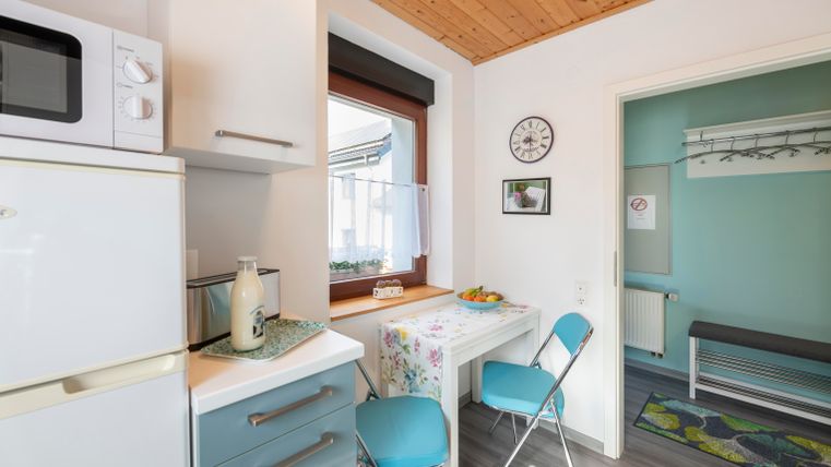 Een moderne keuken met lichte meubels en een kleine tafel. De ruimte is vriendelijk en goed verlicht, met een raam dat naar buiten kijkt.