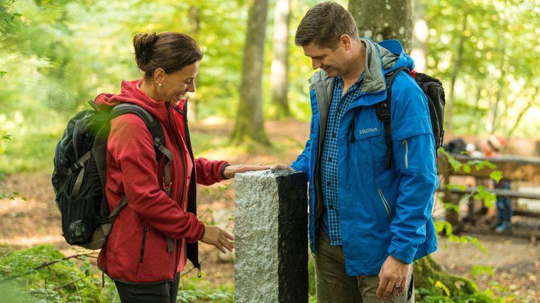 Twee mensen staan in het bos naast een zwart-witte grenssteen.