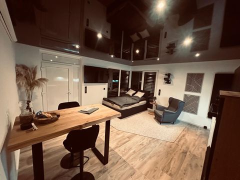 Ein modernes Zimmer mit einem gemütlichen Bett und einem Arbeitsbereich. Das helle Holzfußboden und die stilvolle Beleuchtung schaffen eine einladende Atmosphäre.