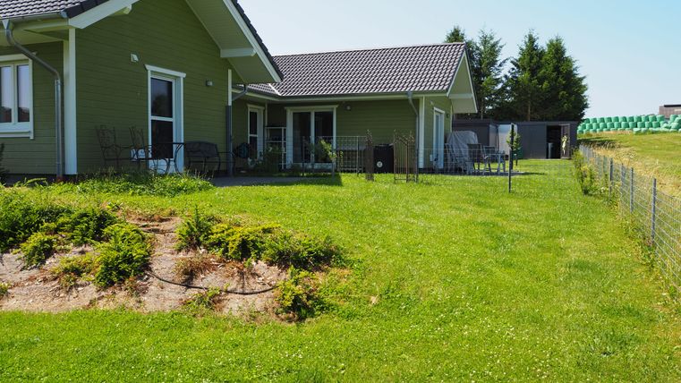 Ein modernes Haus mit grüner Fassade und Garten. Der Rasen ist gepflegt und hat eine Umzäunung.