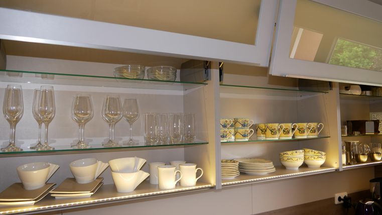 Een moderne keukenvitrine met verschillende glazen en servies. Bovenin staan elegante wijnglazen en daaronder zijn kleurrijke kopjes en borden gerangschikt.