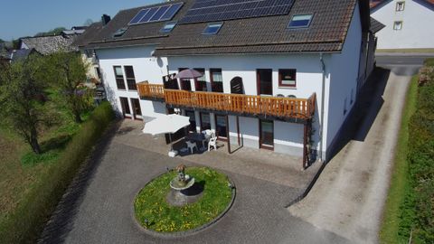Een modern woonhuis met een balkon en zonnepanelen op het dak. De tuin heeft een kleine fontein en ligt in een rustige omgeving.