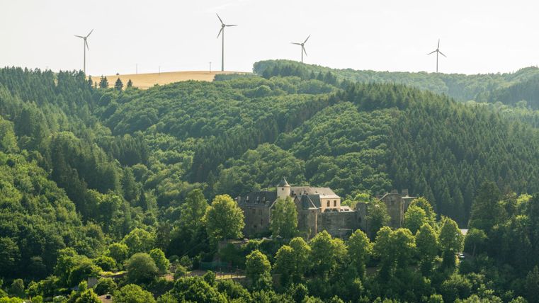 Burg Neuerburg umgeben von Wald und Windrädern im Hintergrund.