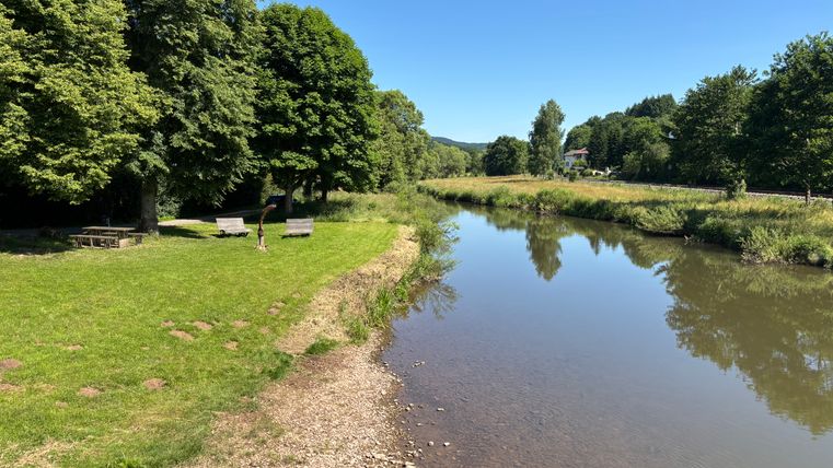 Rivier met groene oever en bomen, persoon op de weide, blauwe lucht.