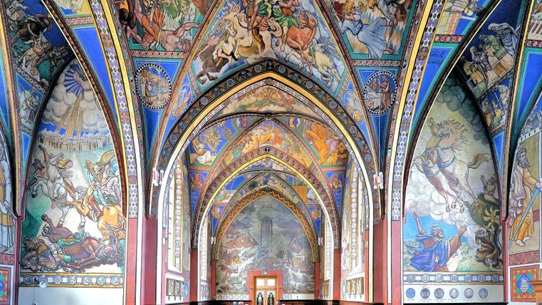 Eine beeindruckende Kapelle mit hohen, gewölbten Decken und bunten Wandgemälden. Die kunstvollen Darstellungen zeigen biblische Szenen und verleihen dem Raum eine festliche Atmosphäre.