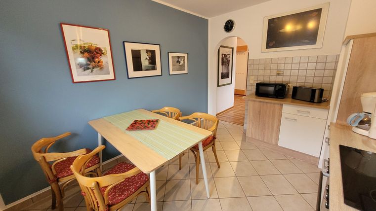 Ein gemütlicher Küchenbereich mit einem Tisch und vier Stühlen. Die Wände sind blau gestrichen, und es gibt mehrere gerahmte Bilder.