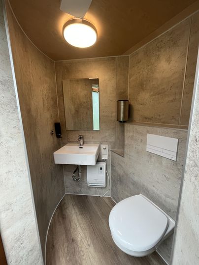 Une salle de bain moderne avec des toilettes et un lavabo. Les murs sont de couleurs neutres et la pièce est bien éclairée.