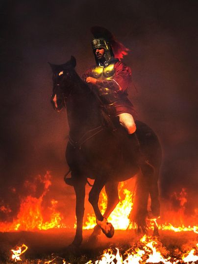 A knight in armor rides a black horse through flames. The background is smoky and dramatic.